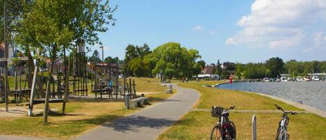 A park with a paved path, playground, and bicycles parked by the water.