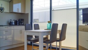 A modern kitchen with white cabinets, a dining table with four chairs, a coffee maker, and a kettle. - Hausboot Schwimmendes Haus in Ribnitz-damgarten (Ribnitz-Damgarten)