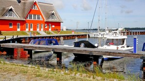 A red building with a thatched roof, a dock with boats, and a calm water body. - Ferienhaus Lotte in Vieregge (Neuenkirchen)