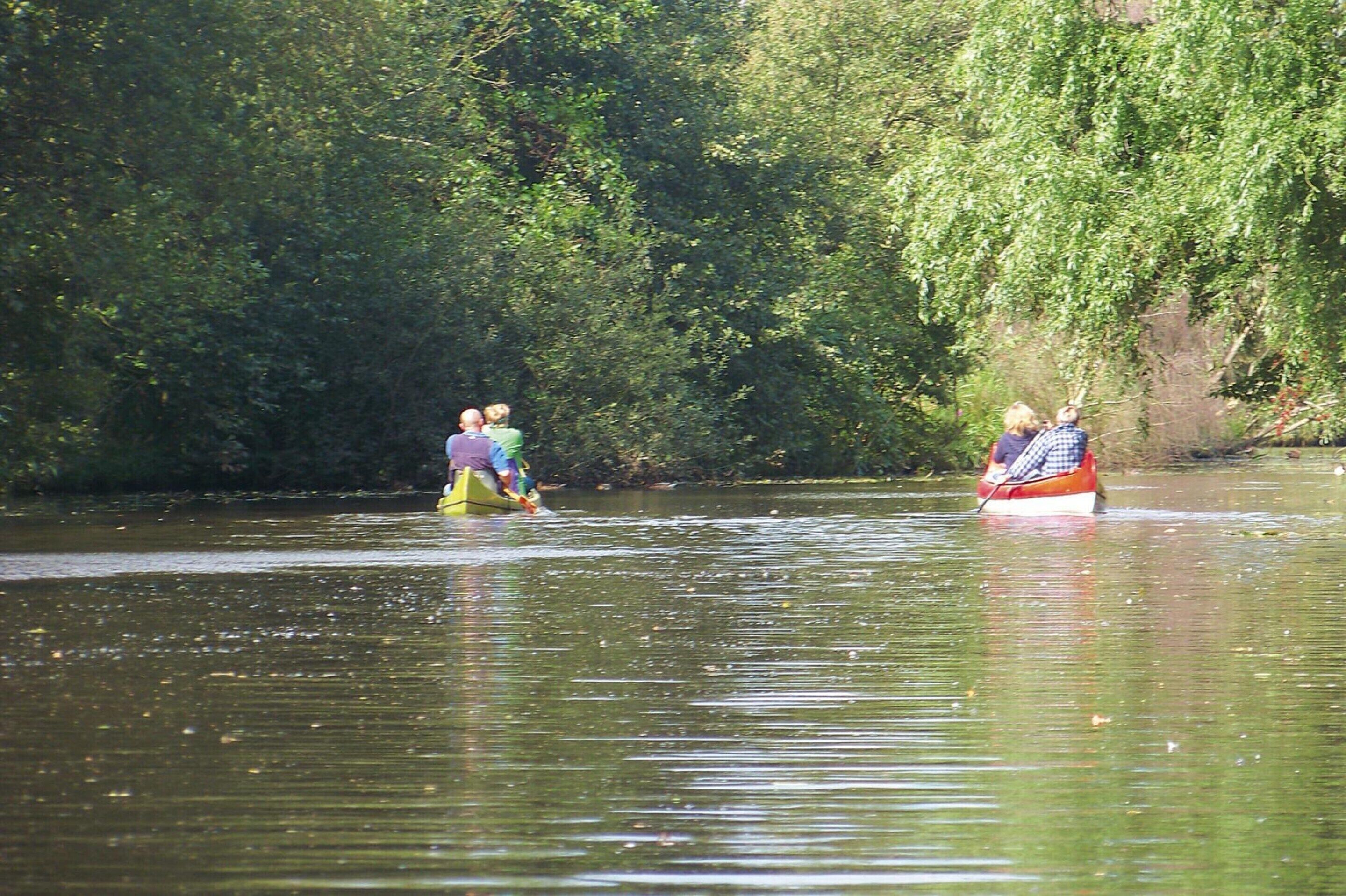 Eine Gruppe von Menschen sitzt in einem Kanu auf einem Fluss, umgeben von dichtem Grün.