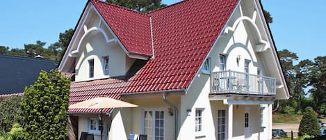 A two-story house with a red-tiled roof, a balcony, and a patio area with outdoor furniture.