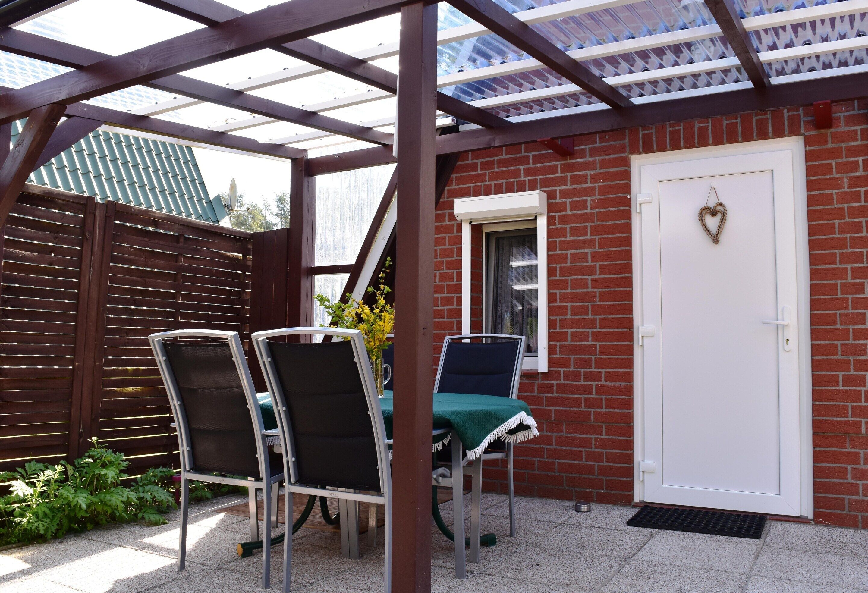 A covered patio with a table and chairs, a door with a heart decoration, and a brick wall.