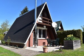 A modern house with a sloped roof, a satellite dish, and a garden with flowers and a wooden planter. - Ferienhaus am Dummer See, Perlin (Perlin)