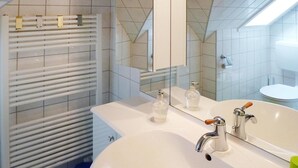 Een badkamer met een witte wastafel, twee kraanwerkers, een spiegel en een handdoekhouder.