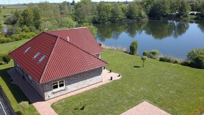 Ein Haus mit rotem Dach, steinernen Fundament und einem Teich im Hintergrund.