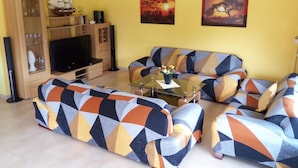 Ein Wohnzimmer mit einer Sofagarnitur, einem Fernseher, einem Schrank und zwei Bildern an der Wand.