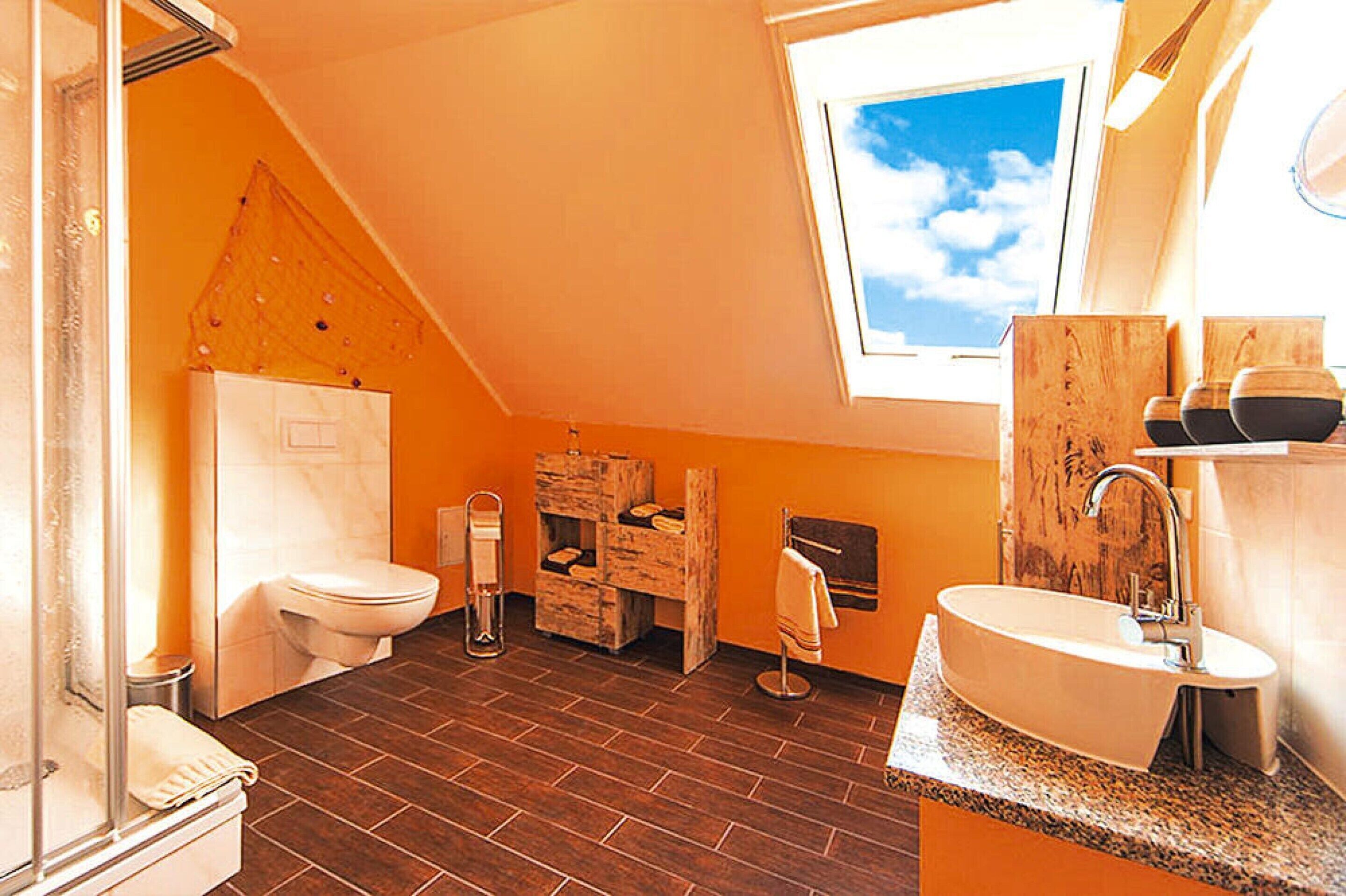 Un baño con techo inclinado, tragaluz, inodoro blanco, armario de madera, lavabo y toallero.