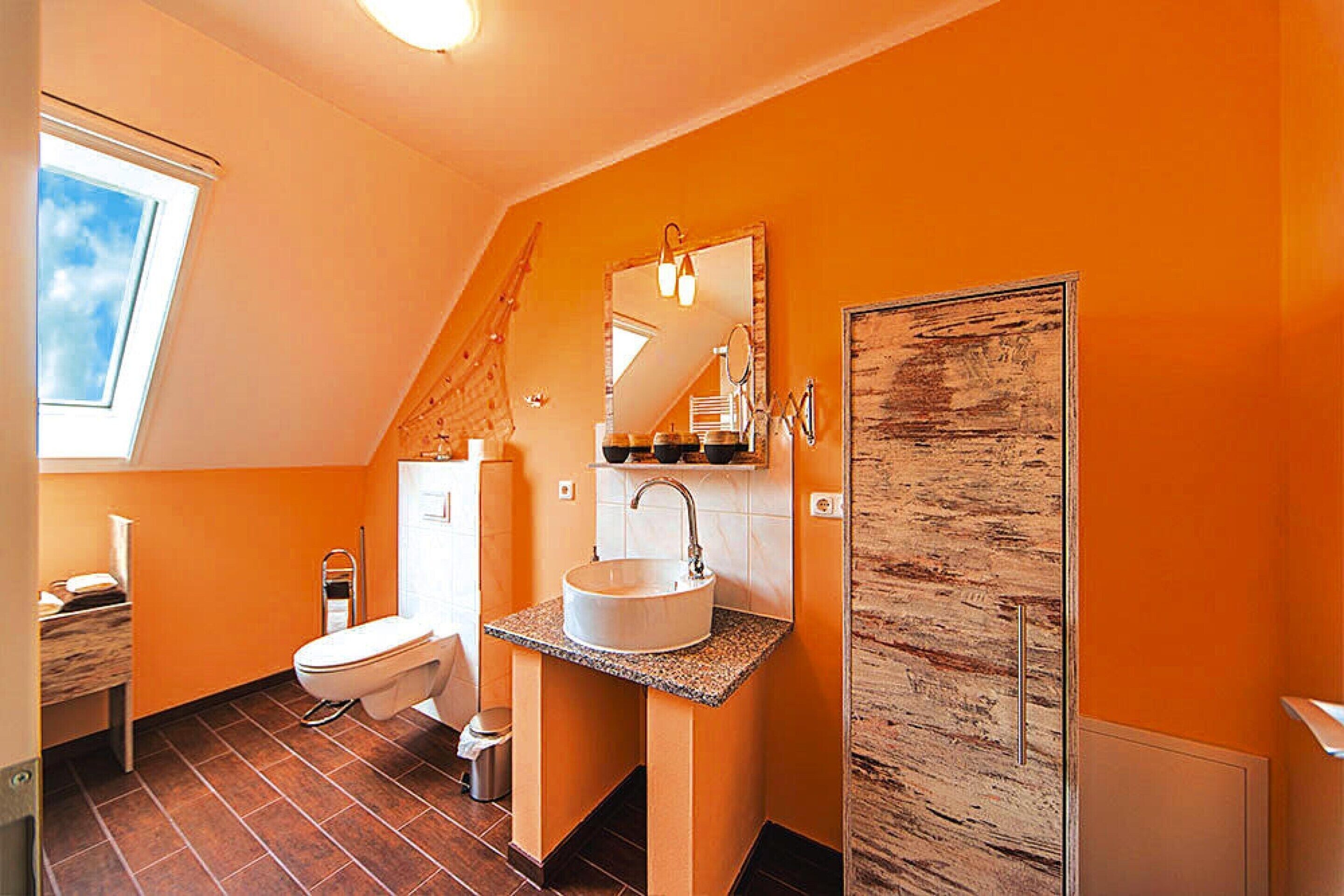 A small bathroom with a skylight, a white sink, a toilet, and a wooden door.