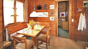 A wooden cabin interior with a dining table set for four, a bench, and a kitchen area visible through an open doorway. - Ferienhauser Lauterdorfle, Hayingen (Hayingen)