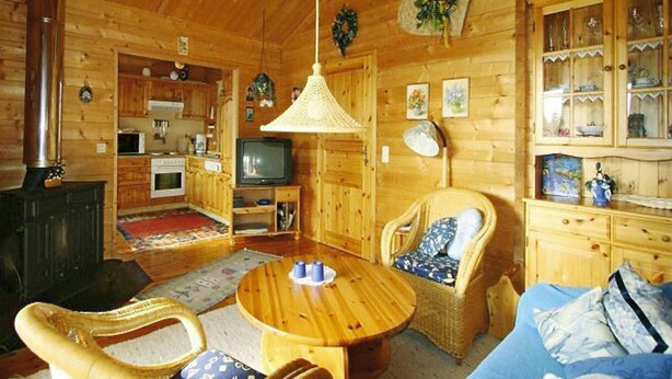 A cozy log cabin interior with a dining area, a television, wicker furniture, and wooden cabinets. - Ferienhauser Lauterdorfle, Hayingen (Hayingen)