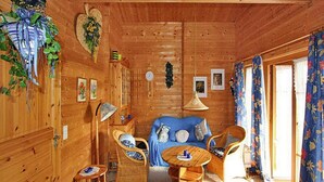A cozy wooden cabin interior with a blue sofa, wicker chairs, a small round table, and a hanging light fixture. - Ferienhauser Lauterdorfle, Hayingen (Hayingen)