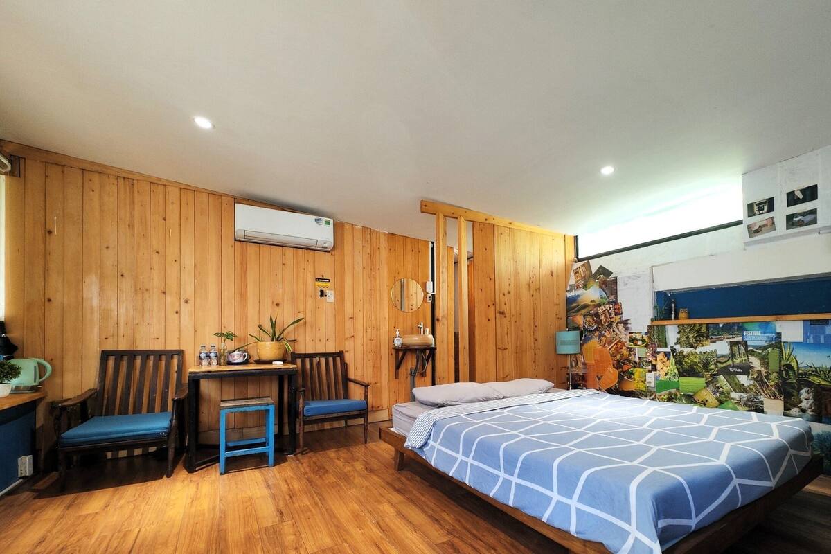 Une pièce aux murs en bois, un lit recouvert d’une courtepointe à motifs bleus, un bureau avec des chaises et un mur orné de divers affiches.