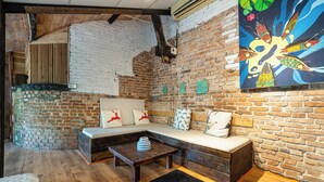 A cozy room with a brick wall, a wooden bench, a small table, and a colorful painting. - HoLo Bato SaiGon - Serviced HomeStay (Ho Chi Minh City)