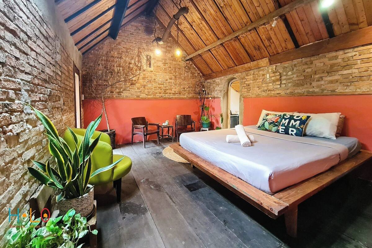 Une pièce rustique avec un plafond en bois, un mur en briques, un lit avec des oreillers, une chaise, une petite table et des plantes en pot.
