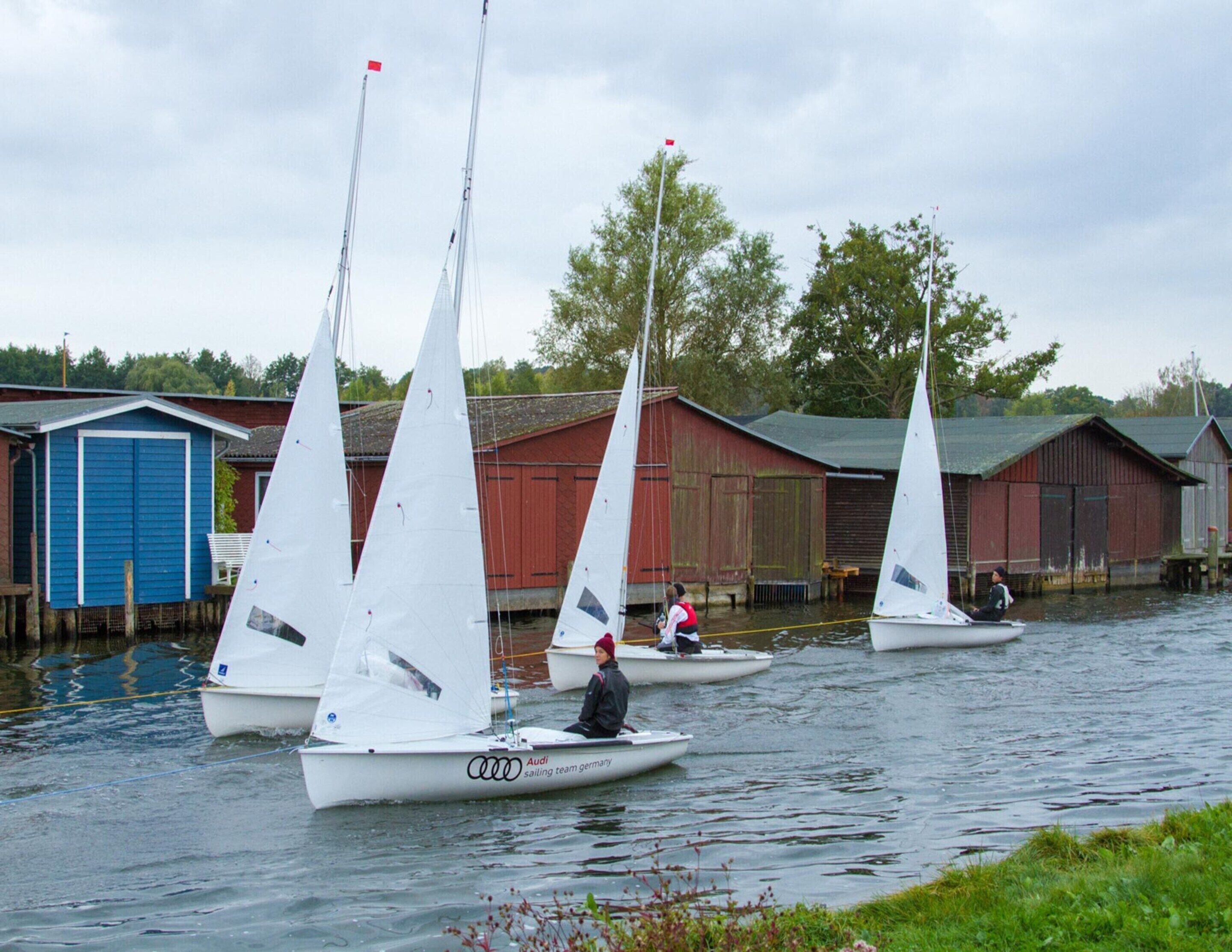 Sailboats on a calm water body with wooden buildings in the background.