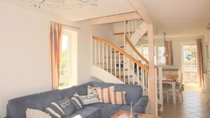 A living room with a blue sofa, a wooden staircase, and a dining area. - Vacation Park Muritz in Rechlin-nord (Rechlin)