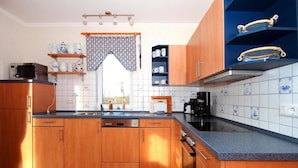 Een moderne keuken met houten kastjes, een zwart aanrecht en een raam met een decoratief gordijn.