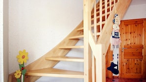 Een houten trap met een leuning, een houten deur en een kleine bloemversiering aan de muur.