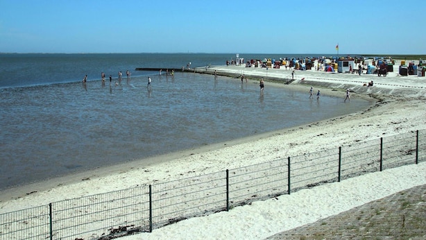 Een strand met zand en een pier, waar mensen zijn.