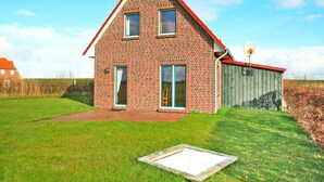 Een tweelaags bakstenen huis met een rood dak, een schotelantenne en een houten tuinhuis in de achtertuin.