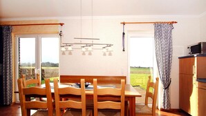 Een eetgedeelte met een houten tafel en stoelen, een plafondlamp en uitzicht door de glazen deur.