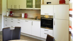 Moderni keittiö, jossa on valkoiset kaapit, musta uuni ja kahvinkeitin.