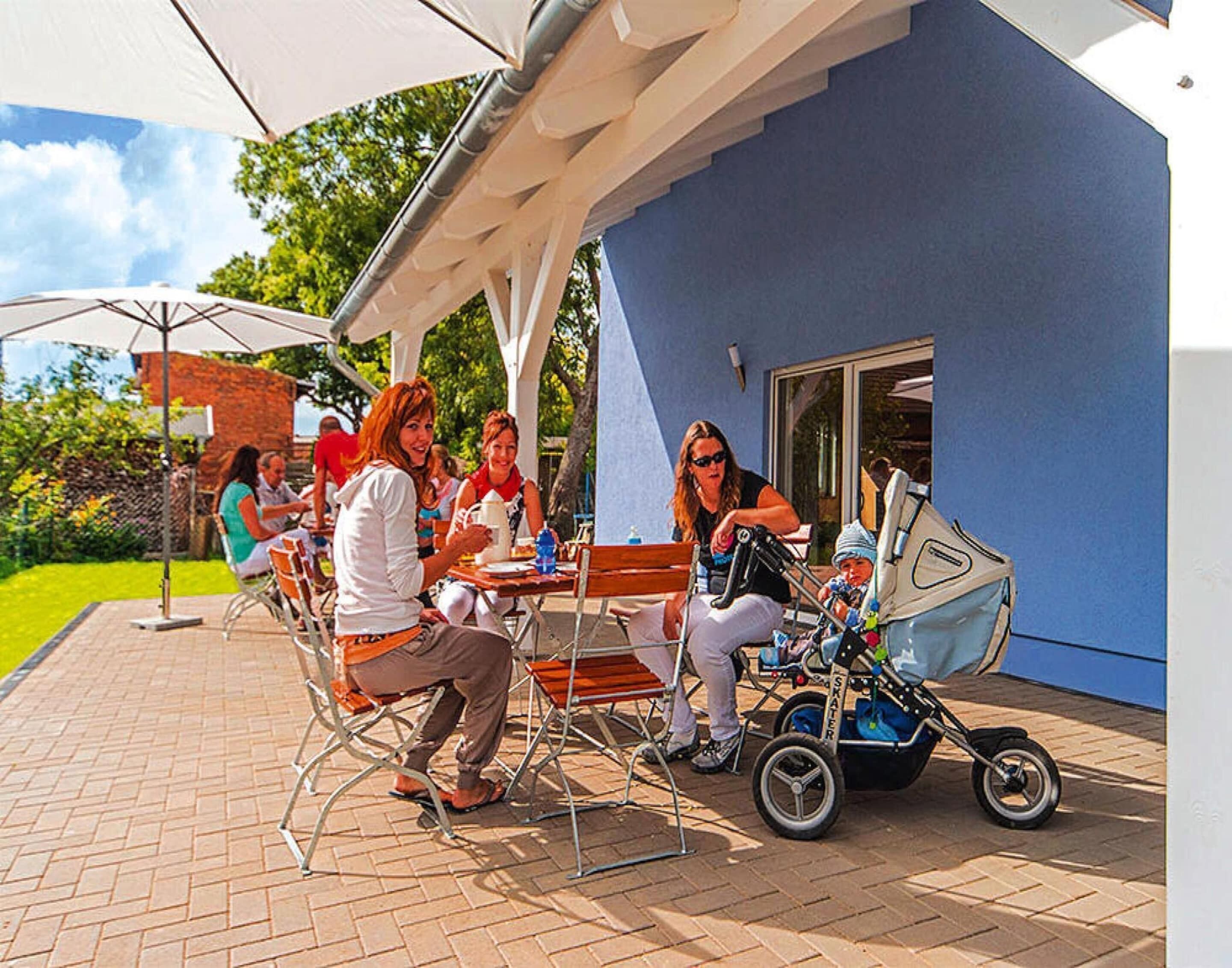 An outdoor patio area with a blue building, outdoor seating, and a stroller.