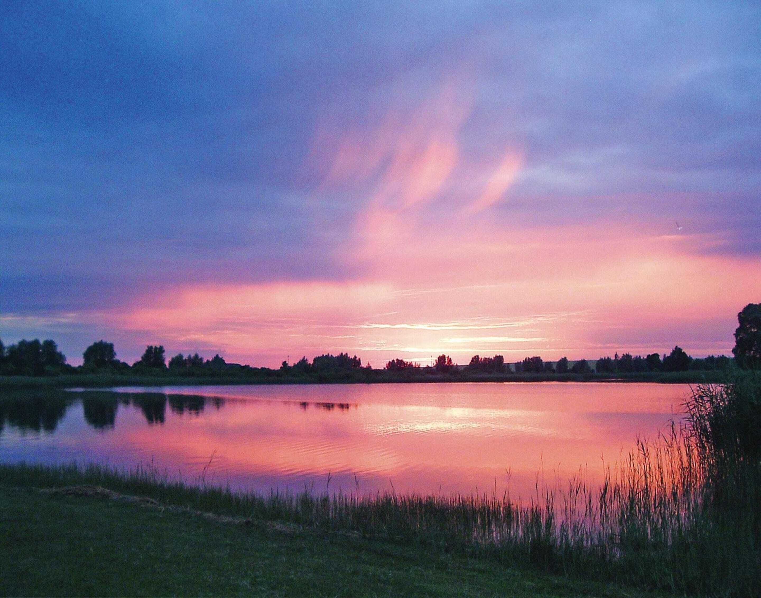 A calm lake at dusk with a clear sky and silhouettes of trees in the background.