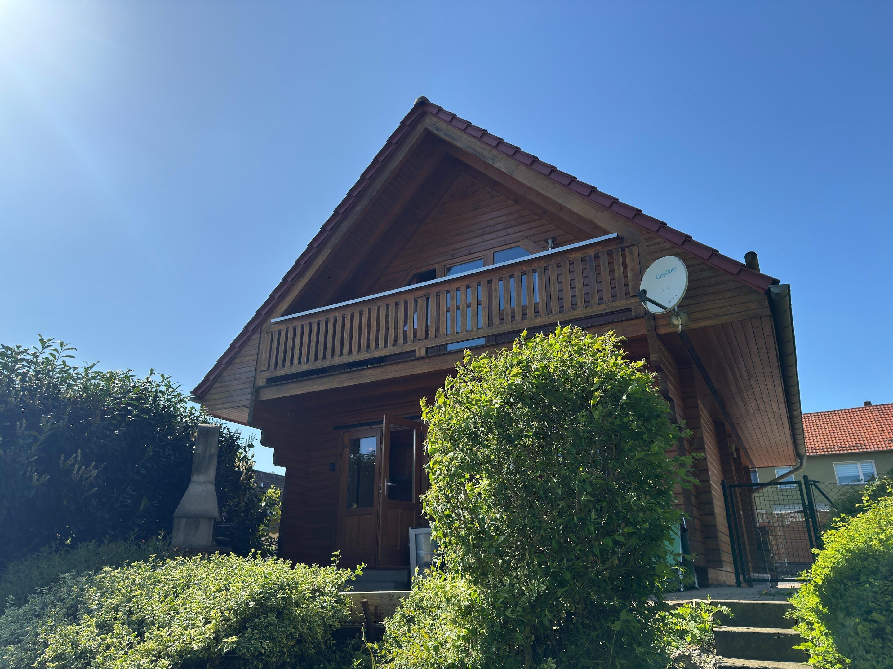 Un chalet en bois doté d’un balcon, d’une antenne parabolique et d’un toit recouvert de tuiles rouges.