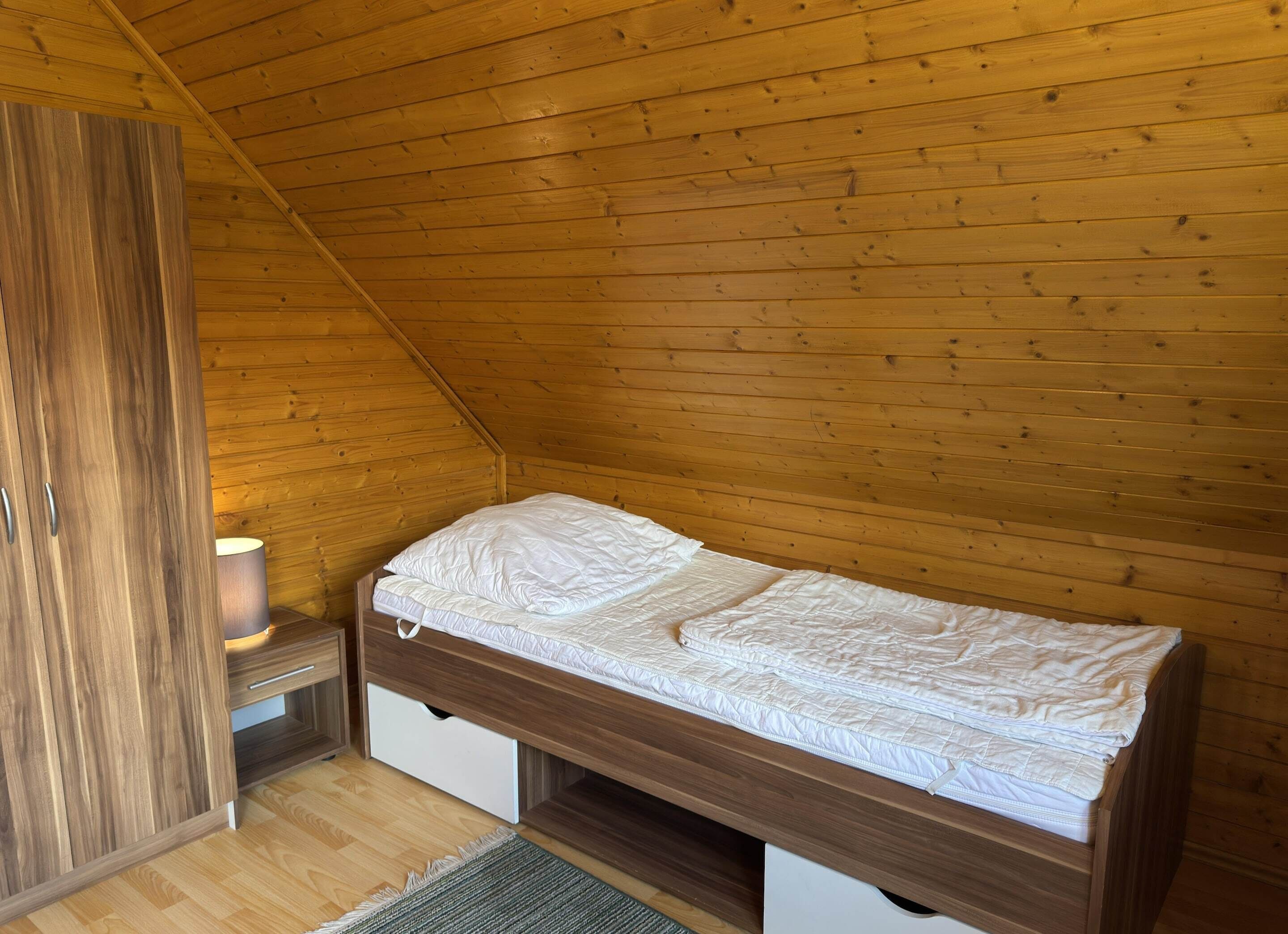 A small, single-bed room with wooden walls and a sloped ceiling.