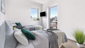 A modern bedroom with two beds, a mounted TV, and large windows offering a view of buildings. - Penthouse Dock 76 Bridge - waterfront location, roof terrace, sea view, sauna (Olpenitz)