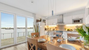 Eine moderne Küche mit großem Esstisch, gedeckt für sechs Personen, Blick auf das Wasser und einem Balkon mit Geländer.