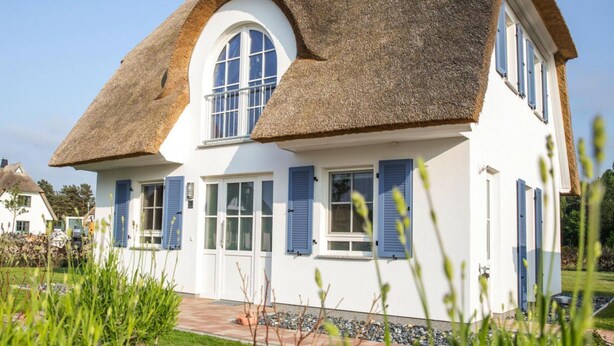 A house with a thatched roof, white walls, and blue shutters. - Luxushaus Boddenkuste mit Sauna (Fuhlendorf)