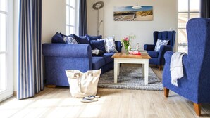 A living room with a blue sofa set, a coffee table, and a painting on the wall. - Luxushaus Boddenkuste mit Sauna (Fuhlendorf)