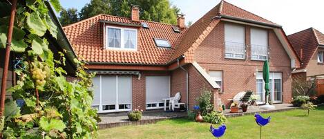 A two-story house with a brick exterior, a tiled roof, and a small front yard with a lawn, a bird sculpture, and a garden.