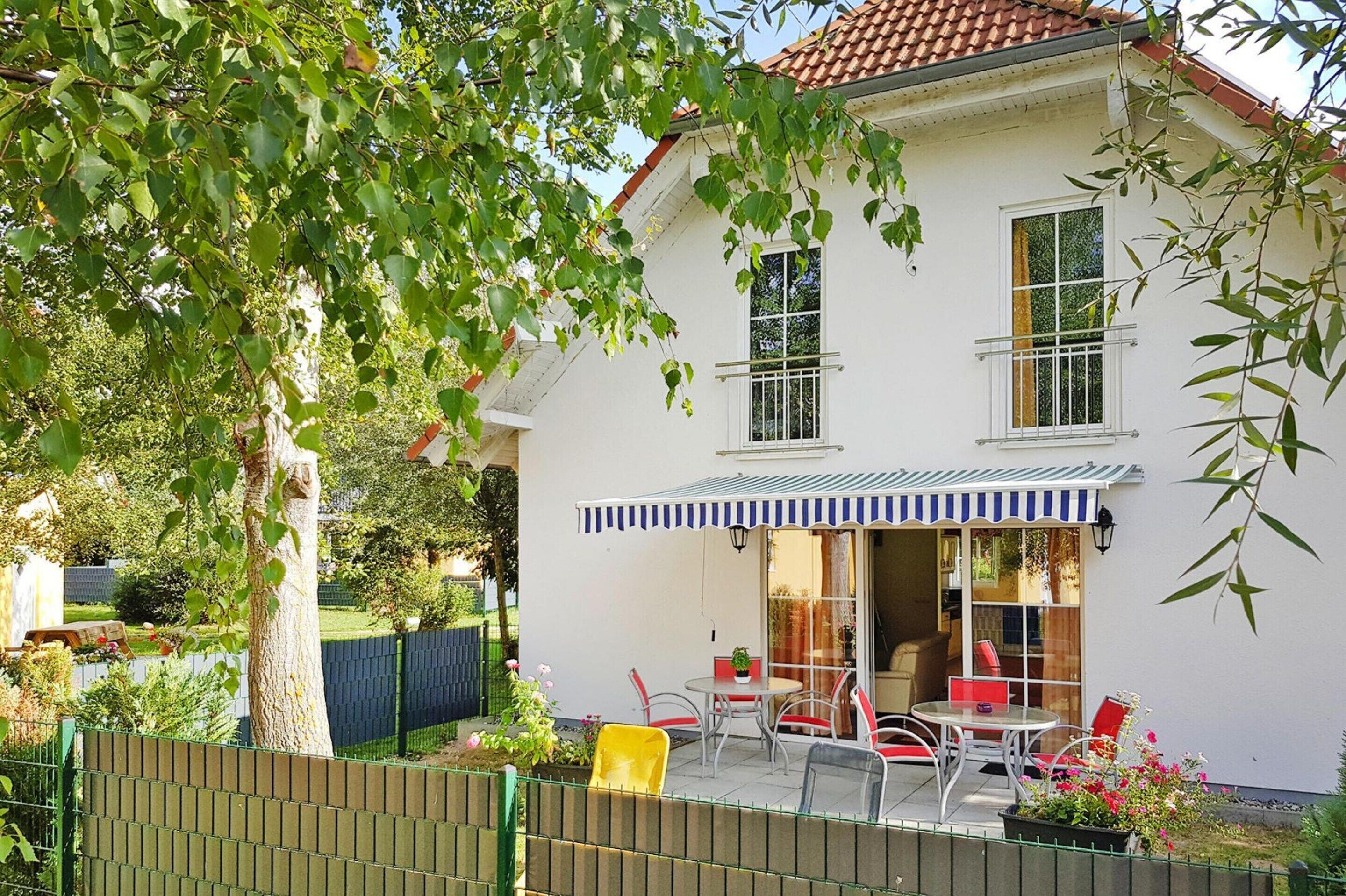 A two-story house with a patio area featuring a table and chairs, a covered seating area, and a fenced garden.