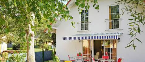 A two-story house with a patio area featuring a table and chairs, a covered seating area, and a fenced garden.