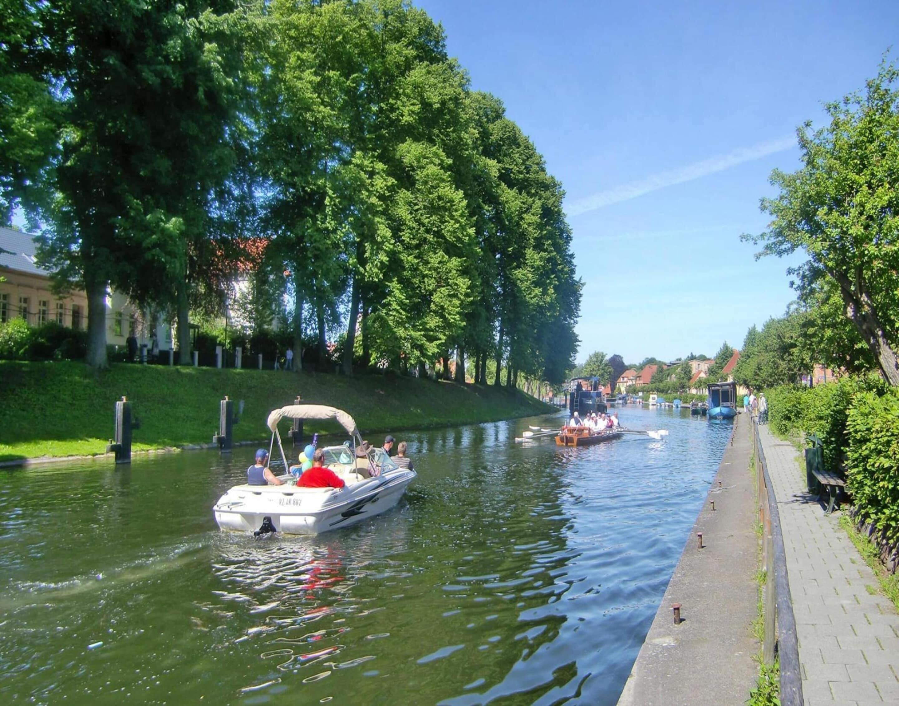 A canal with boats, a paved walkway, and trees.