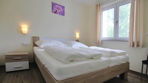 A bedroom with a wooden bed, two bedside tables, a night light, and a window with curtains. - Appartement Hafenflair am Plauer See (Plau am See)