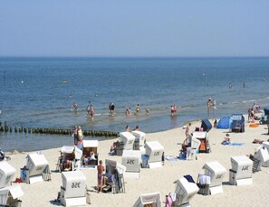 A beach with beach chairs and umbrellas, some people swimming and walking in the water. - Ferienhaus Mein Ankerplatz, Zirchow (Zirchow)