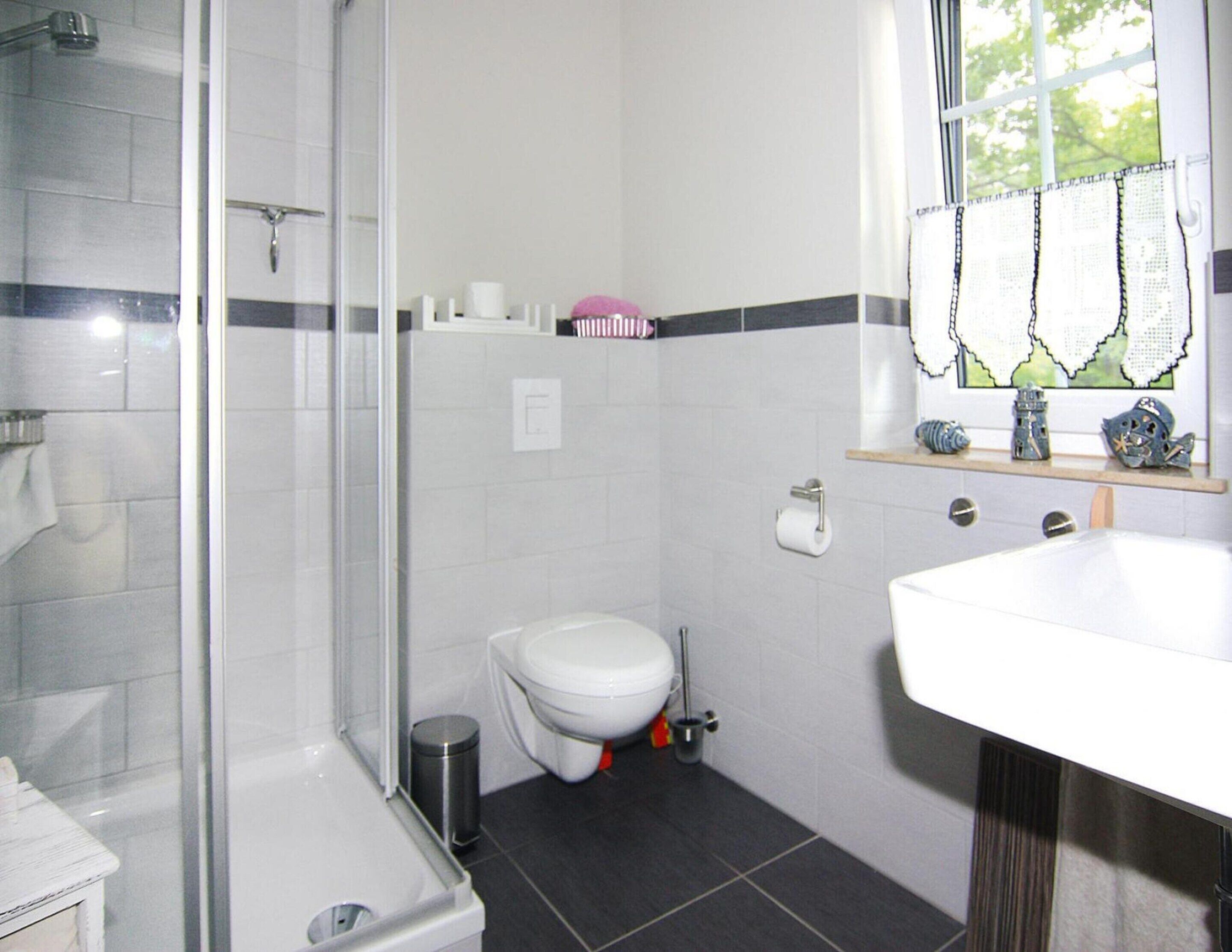 Un baño moderno con cabina de ducha de vidrio, inodoro blanco y lavamanos con espejo.