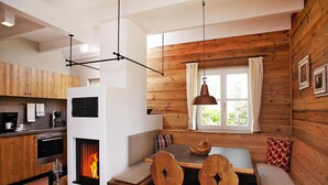 A cozy cabin interior with a fireplace, wooden dining table, and chairs, and a kitchen area with modern appliances.