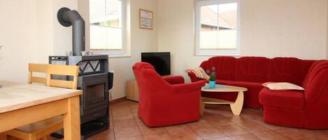 Uma sala de estar com lareira, televisão, sofá vermelho e mesa de madeira.