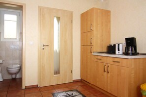 Una cocina pequeña con armarios de madera, una cafetera y un inodoro visible en el baño contiguo.