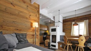 Quarto aconchegante com cama, parede de madeira, cozinha e mesa de jantar com cadeiras.