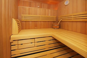 Uma sauna de madeira com bancos, um balde e um termômetro fixado na parede.