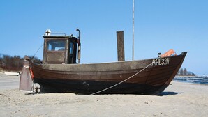 En träbåt med registreringsnummer "RHL 32N" ligger på en sandstrand.