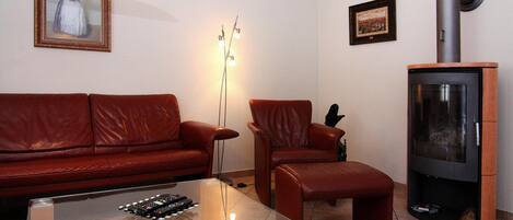 Una sala de estar con un sofá de cuero rojo, una mesa de centro de vidrio, una lámpara de pie moderna, una chimenea empotrada en la pared y un cuadro enmarcado.