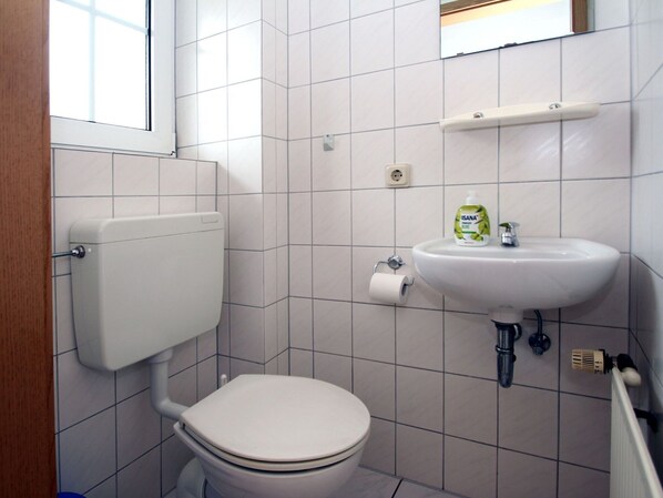 A small bathroom with a toilet, sink, and a window. - Ferienhaus in Nessmersiel (Dornum)