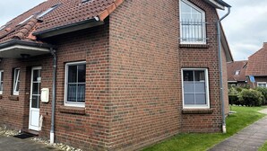 A two-story brick house with a tiled roof, a front door, and a small front yard. - Ferienhaus in Nessmersiel (Dornum)